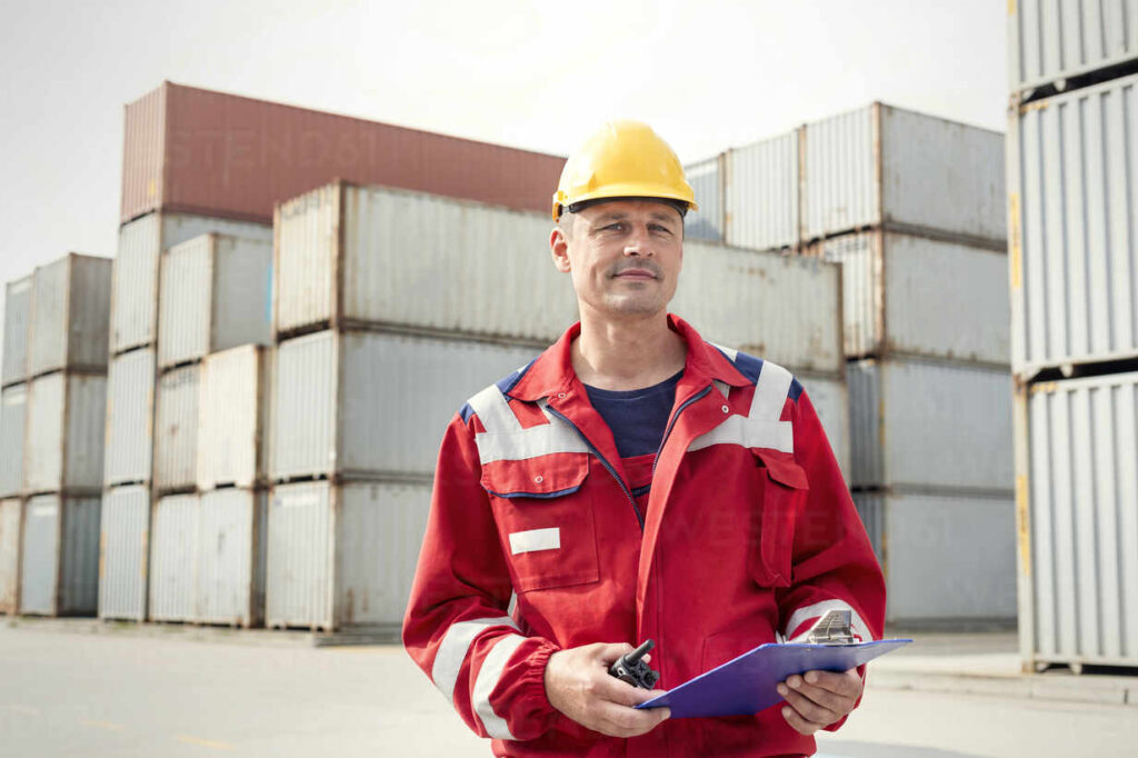 portrait-confident-dock-worker-with-clipboard-and-walkie-talkie-at-shipyard-CAIF25103